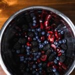 Top-down shot of a mixed berry salad with blackberries, blueberries, and cherries tossed and glistening.
