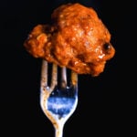 Crispy buffalo cauliflower in air fryer that's been cooked to golden perfection, speared on a fork with sauce dripping, set against a dark background.