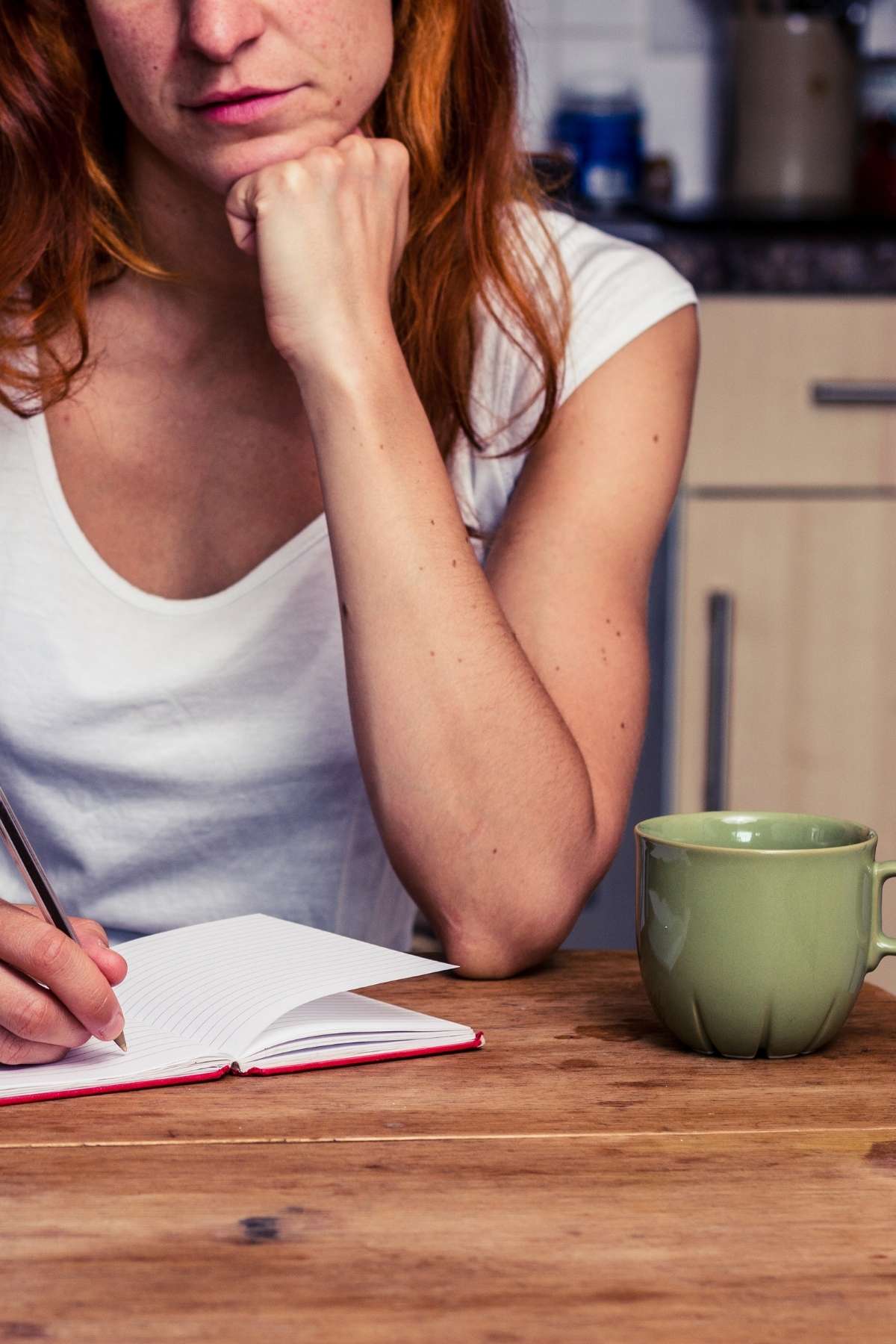 Person writing in a notebook with a cup of coffee, planning bulk foods for meal prep.