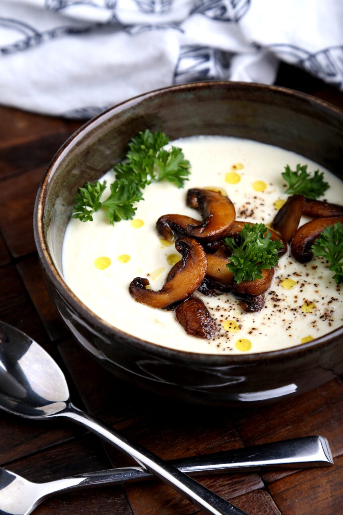 Bowl of creamy vegan cauliflower and cashew soup garnished with mushrooms and herbs.