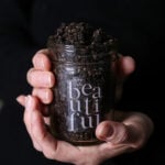 Two hands holding a glass mason jar of coffee sugar scrub.