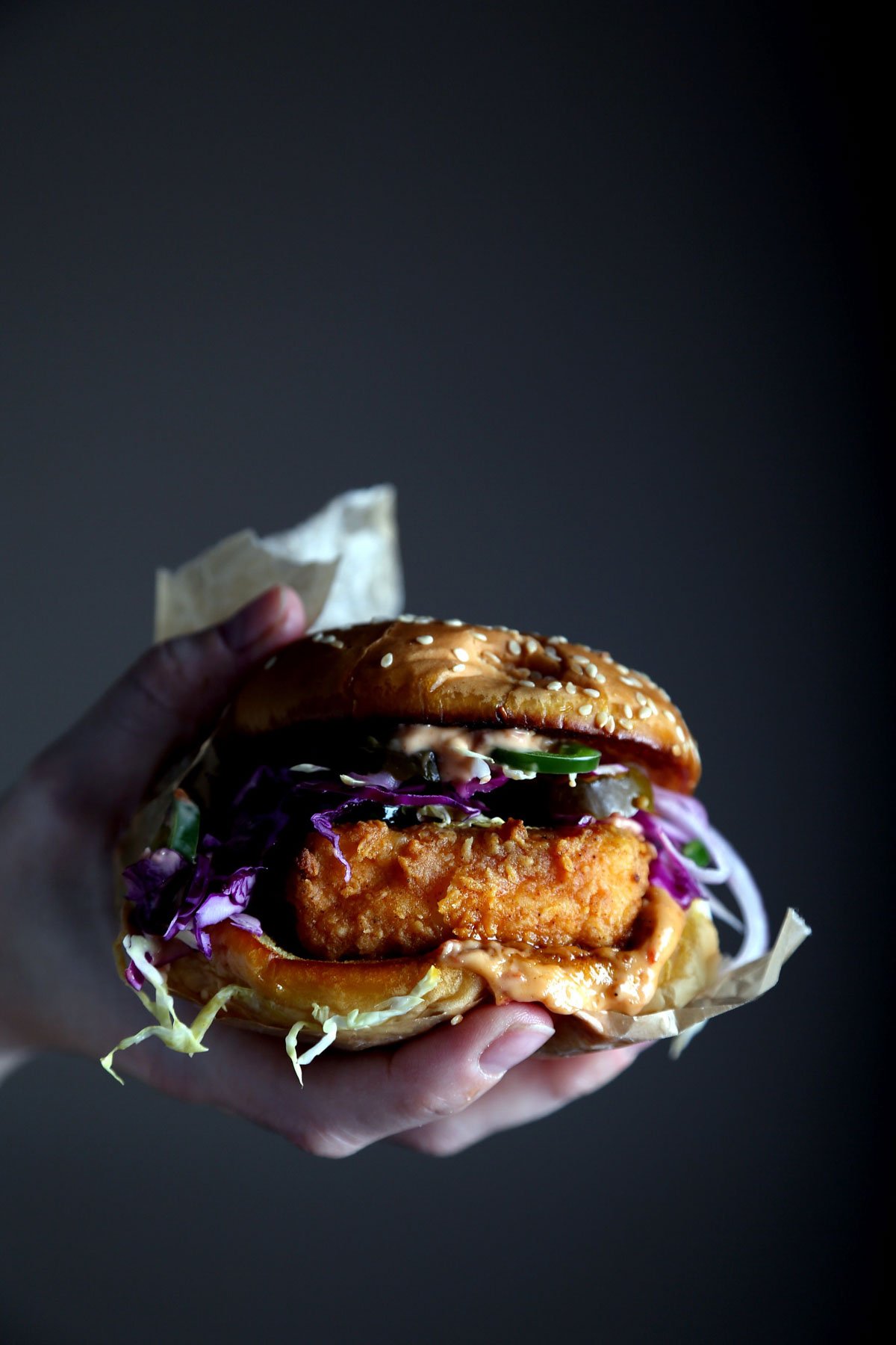 A hand holding a crispy fried tofu sandwich.