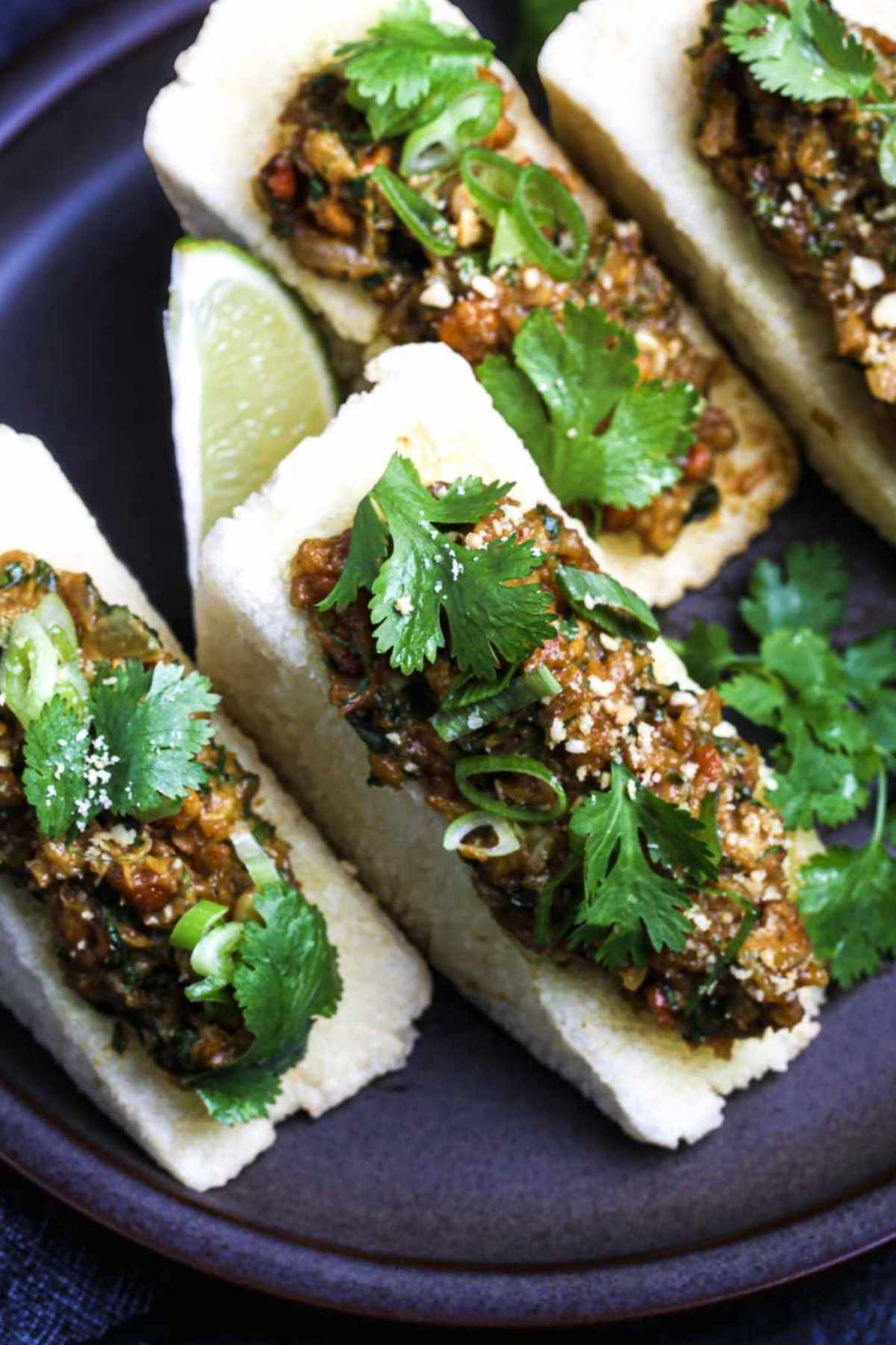 Top-down view of crispy fried tofu triangles filled with lemongrass–peanut sauce, garnished with cilantro, scallions, and lime on a dark plate.