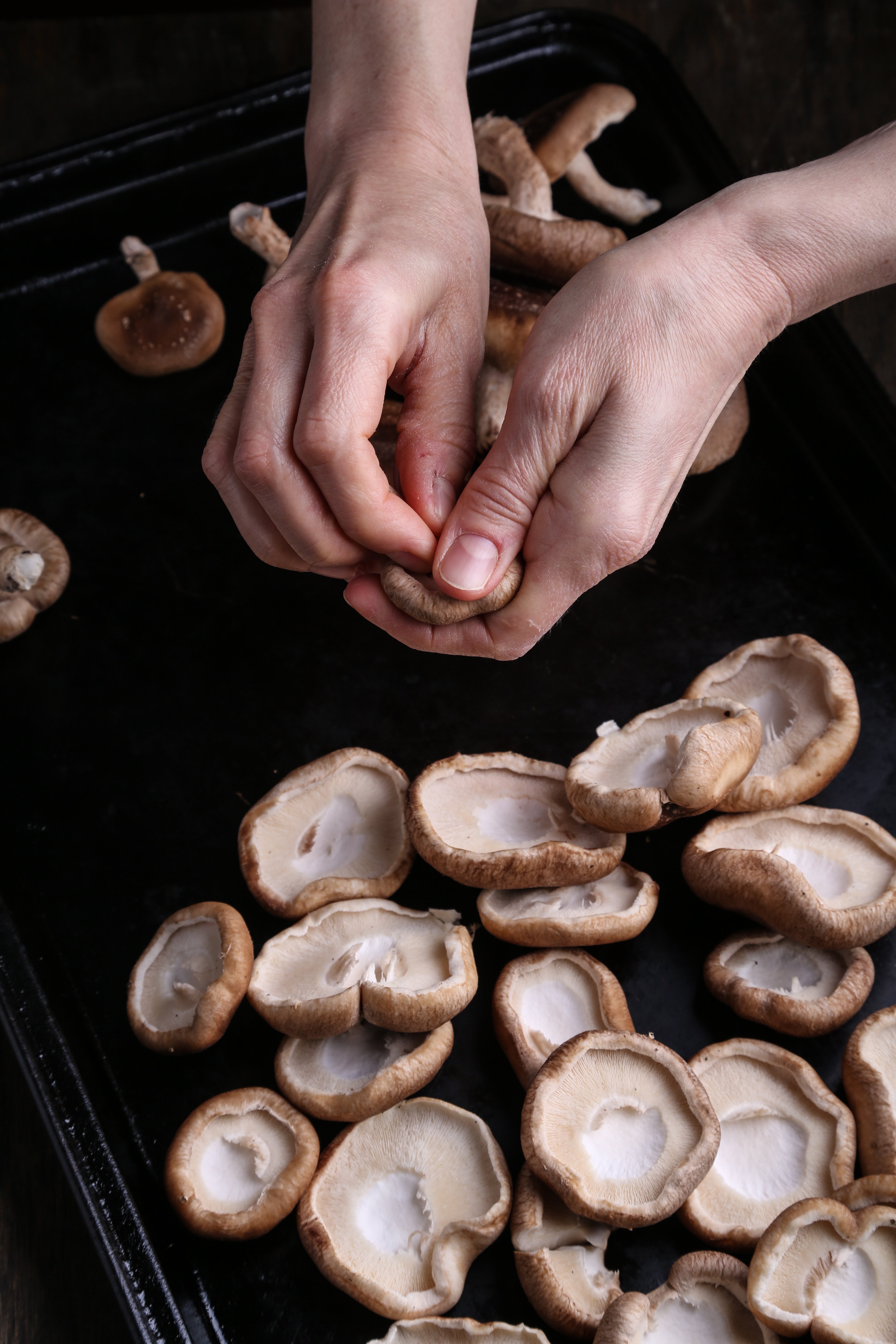 Two hands destemming shiitake mushrooms.