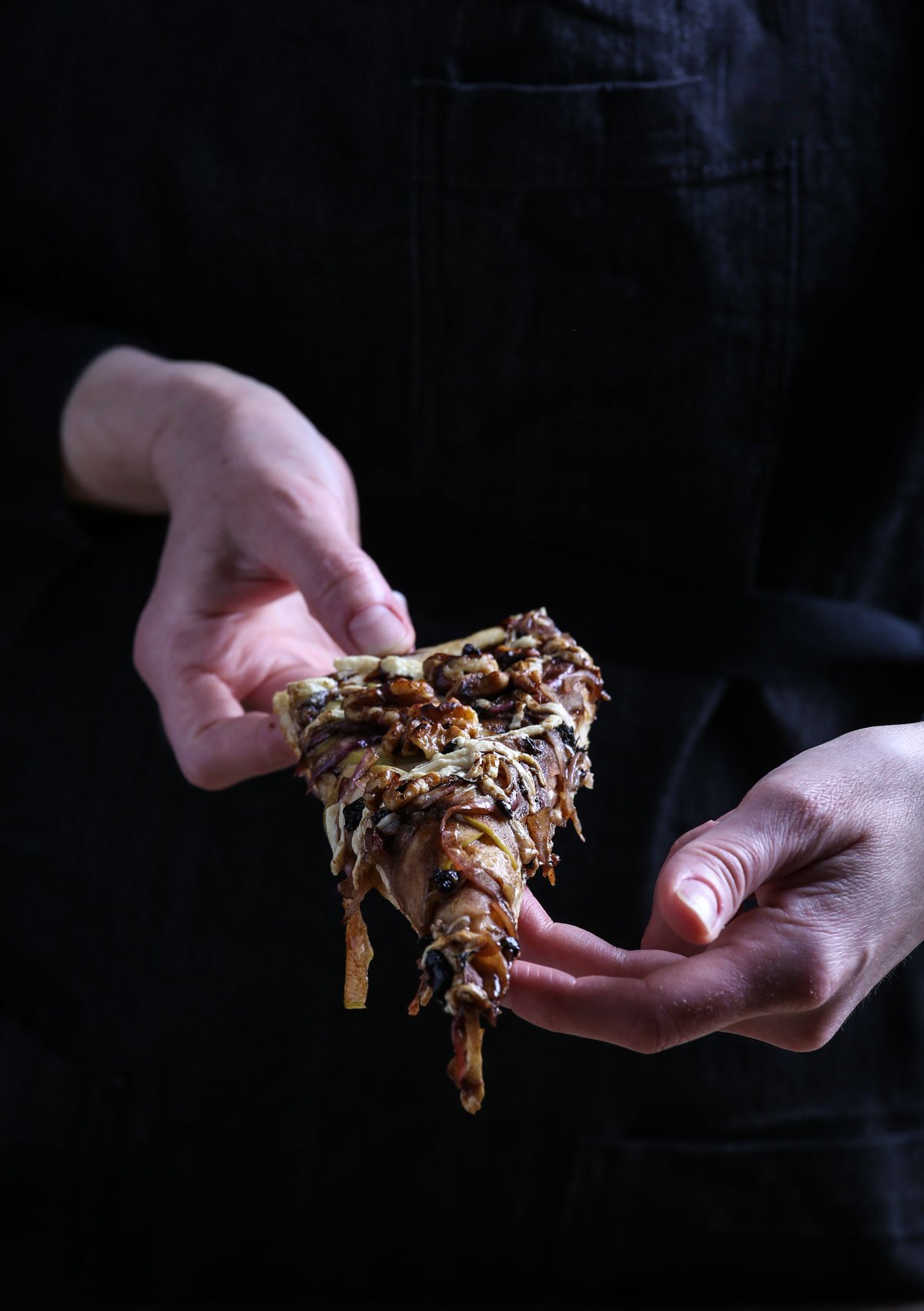 Hands holding up a slice of focaccia pizza.