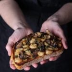 Two hands holding a piece of garlic confit and mushroom toast.
