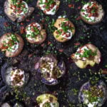 A top-down shot of loaded smashed potatoes on a baking sheet.