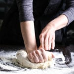 Hands kneading vegan pizza dough on a floured tabletop.