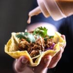 Hand drizzling chipotle-lime sauce over crispy oyster mushroom tacos filled with cabbage and cilantro.