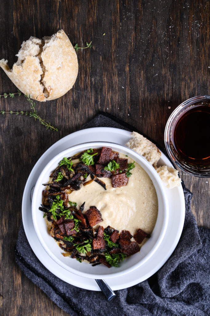 A bowl of creamy roasted parsnip soup in a white bowl against a dark wood background.