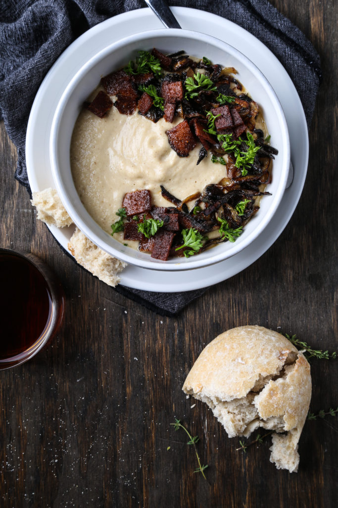 A bowl of creamy roasted parsnip soup garnished with vegan bacon and parsley.