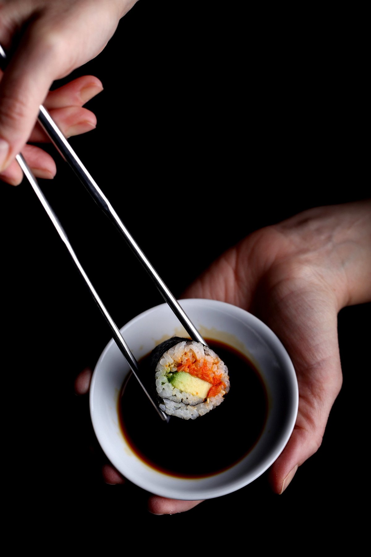 Spicy carrot lox sushi, held with chopsticks.