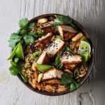 Overhead shot of a ramen bowl with seared tofu, lime wedges, and fresh herbs for a spicy tofu ramen noodles recipe.