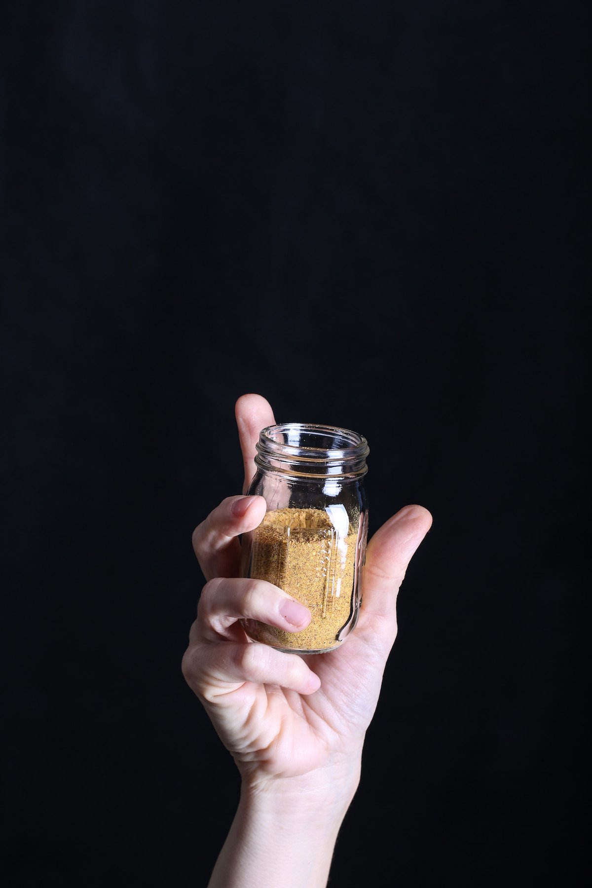A hand holding a small jar of sriracha-nooch seasoning.