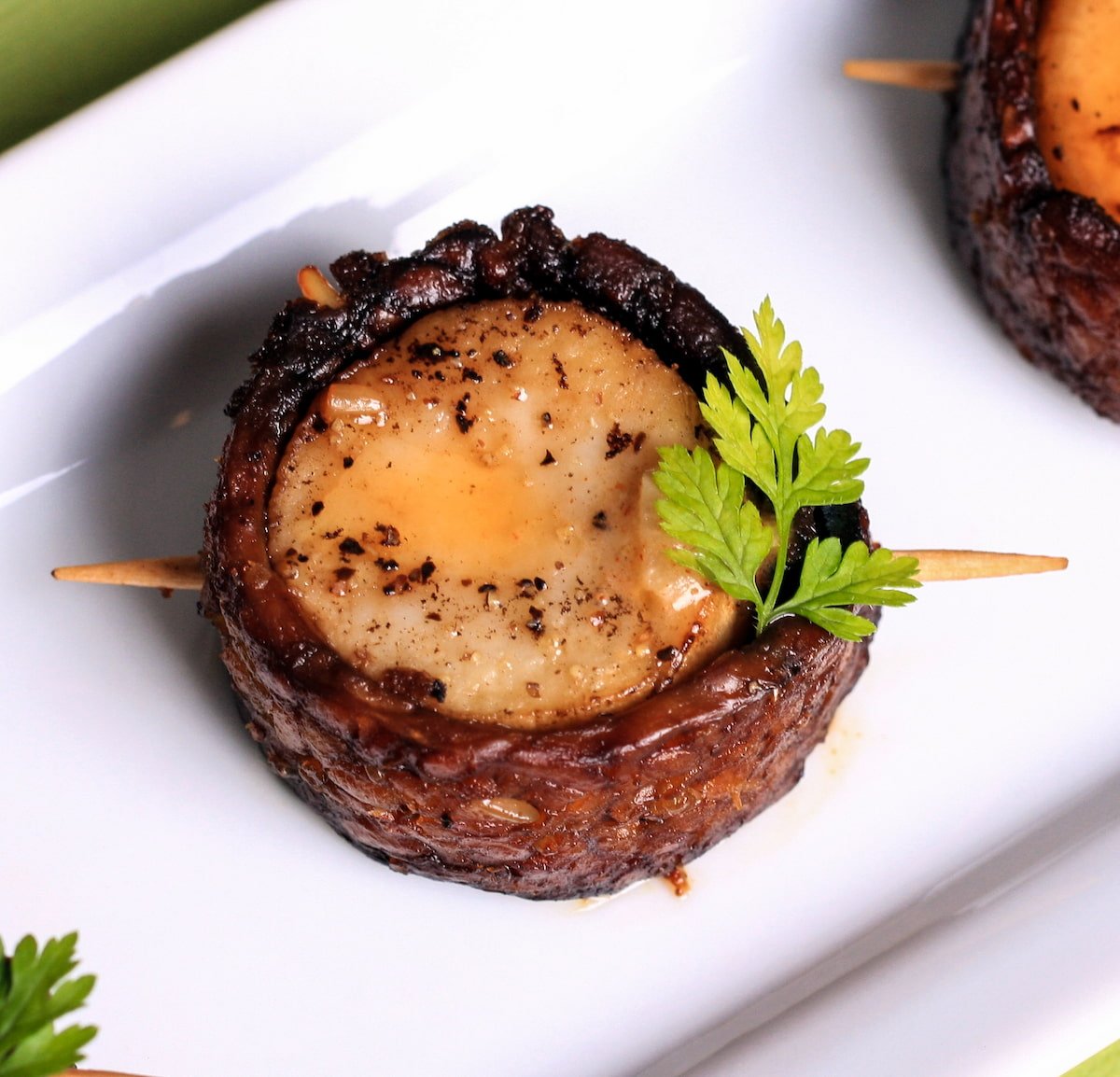 A vegan bacon-wrapped scallop with garnish.
