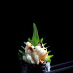 A crispy enoki mushroom roll, held with chopsticks.