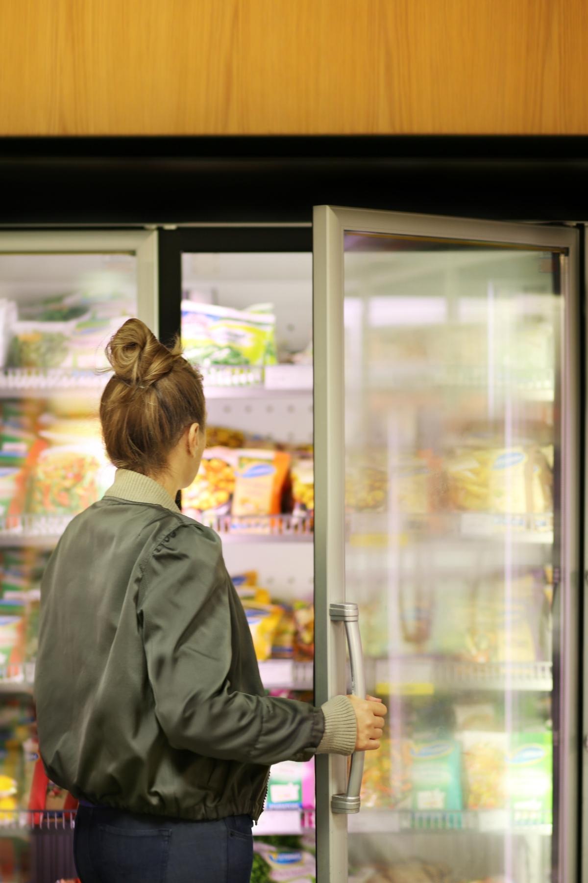 A woman standing in the freezer aisle of a grocery store with the door open.