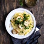 A plate of linguine topped with smoky cashew cream sauce, seared king oyster mushroom scallops, and fresh parsley, served with white wine.