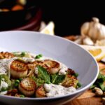 A bowl of vegan scallops made from seared king oyster mushrooms, served over pasta with peas, mint, and dairy-free sauces.