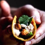 Close-up of a hand holding a smoky roasted cauliflower taco filled with avocado, cilantro, and drizzled chipotle sauce.
