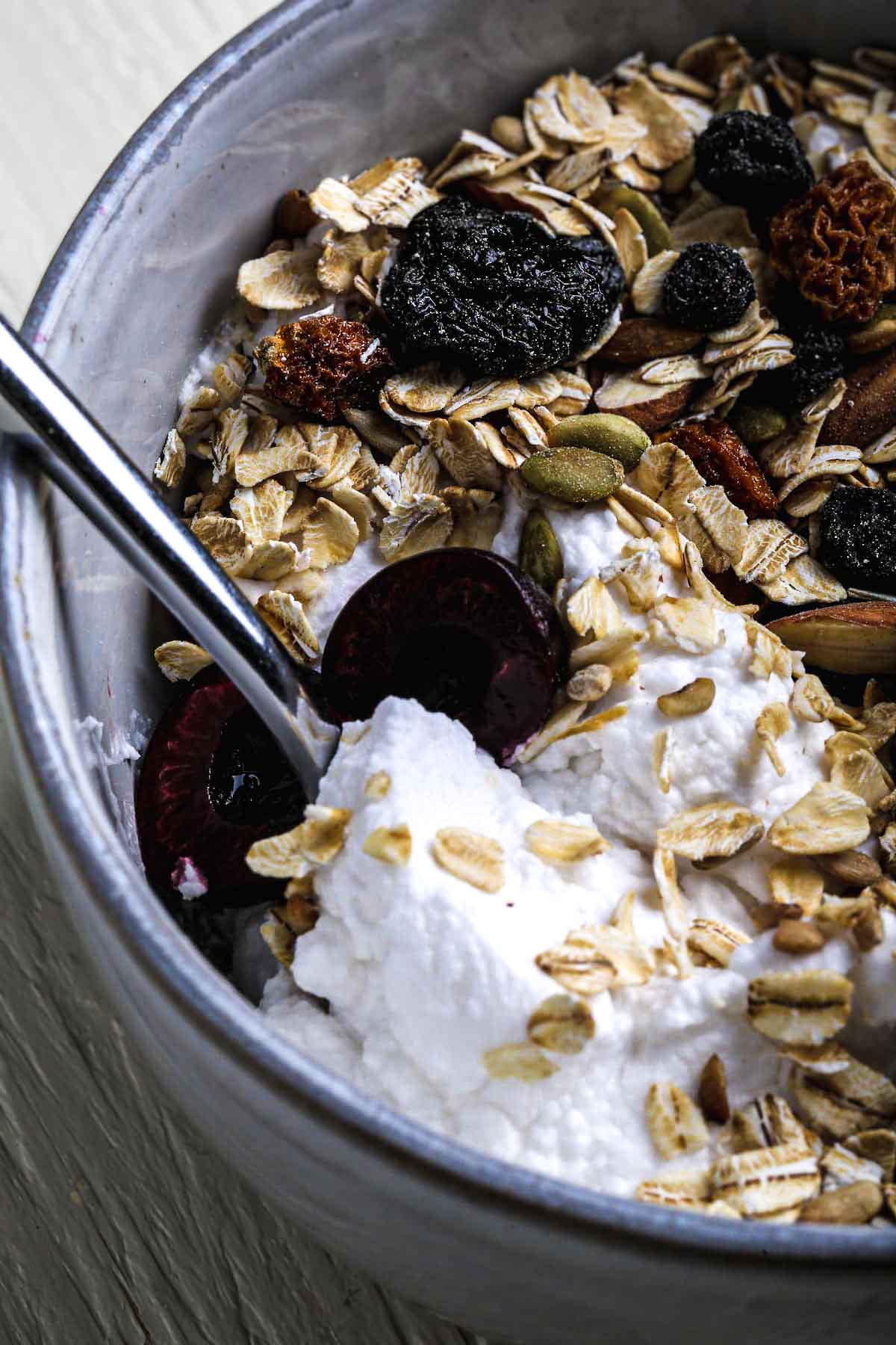 A bowl of creamy homemade vegan yogurt topped with muesli, dried fruit, and fresh cherries.