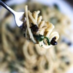 A close-up of a fork twirling pasta coated in a silky white wine sauce with garlic, parsley, and olives.